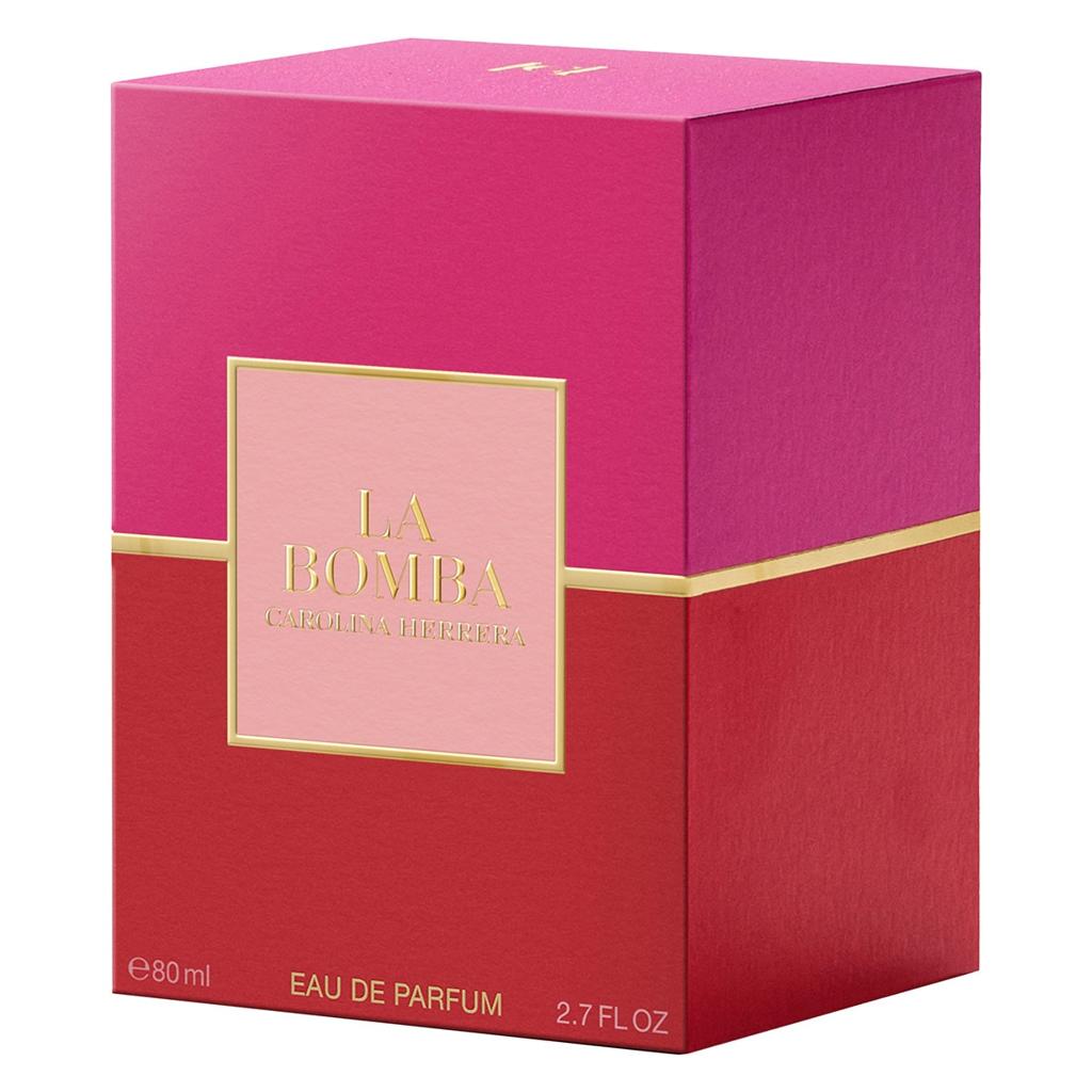 La Bomba Eau de Parfum box by Carolina Herrera, featuring a vibrant magenta top half, a deep red bottom half, a gold horizontal stripe, and a central light pink label with gold lettering.