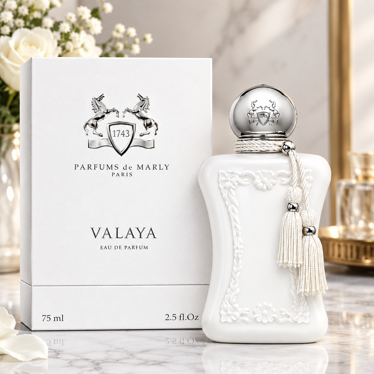 A white perfume bottle with an ornate embossed floral design and a silver spherical cap stands beside its white branded box. The bottle has a cream tassel hanging from the cap.