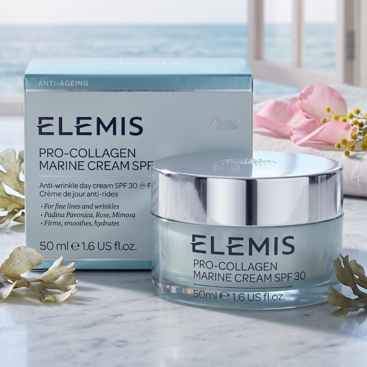 Elemis Pro-Collagen Marine Cream SPF 30 shown with its light blue and white product box and a clear jar with a reflective silver lid, styled on a marble surface with soft pink and white flowers.